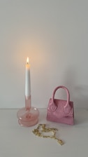 A stylish handbag resting on a wooden table next to a glowing candle.