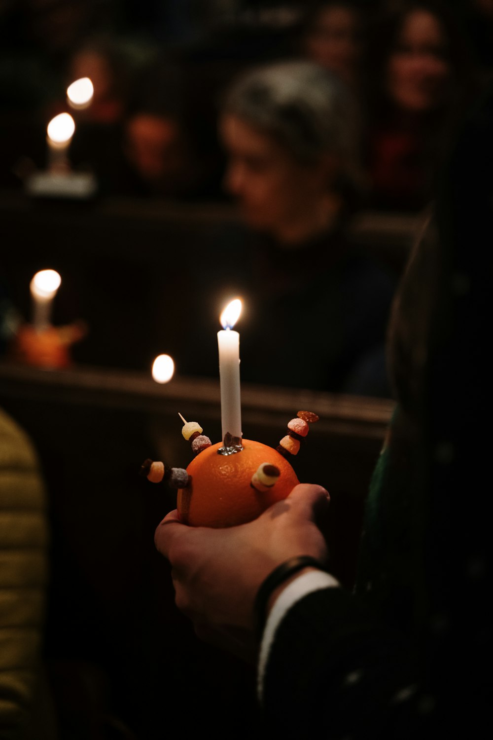 a person holding an orange with candles in the background