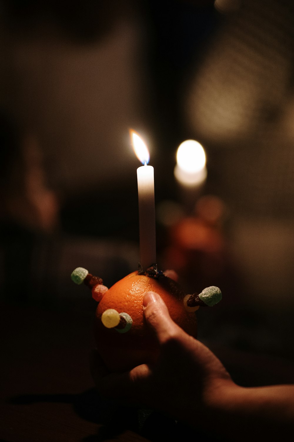 a hand holding an orange with a candle in it