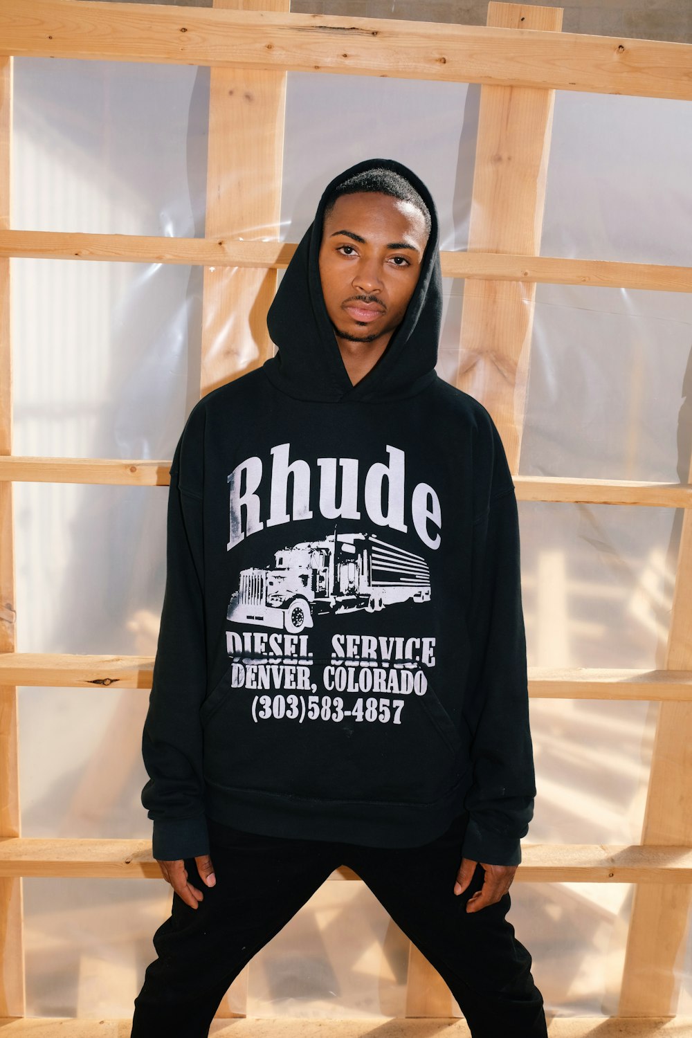 a man standing in front of a wooden wall wearing a black hoodie