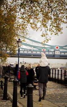 a group of people walking down a sidewalk next to a bridge