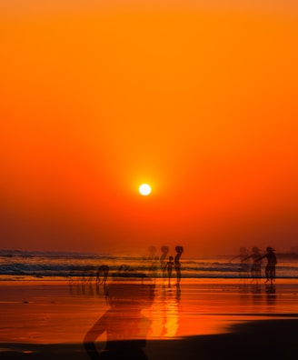 a group of people standing on top of a beach under a sunset