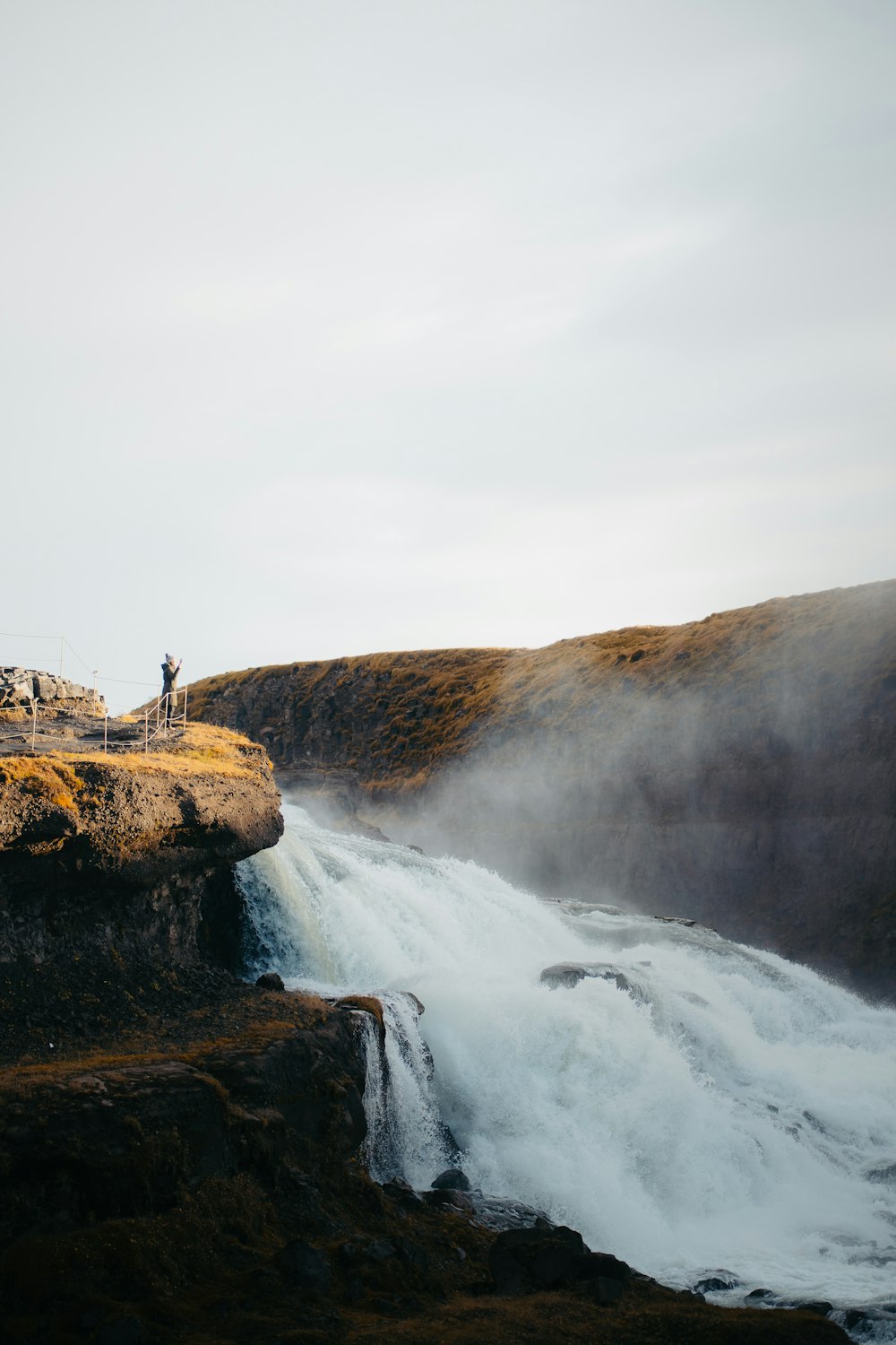 two people standing on a cliff above a waterfall