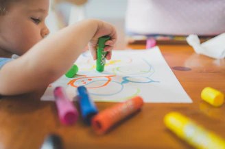 a little boy that is sitting at a table with some crayons