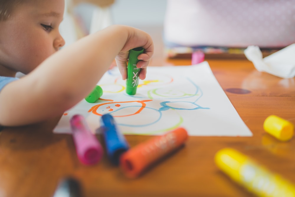 Un niño pequeño que está sentado en una mesa con algunos crayones