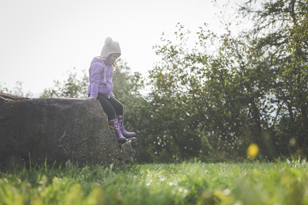 a little girl sitting on a rock in the grass