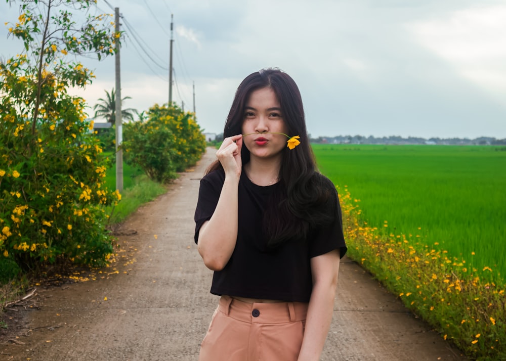 a woman with a flower in her hand standing on a dirt road