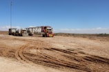Dramatic shot of mining trucks moving through dusty terrain under a cloudy sky.
