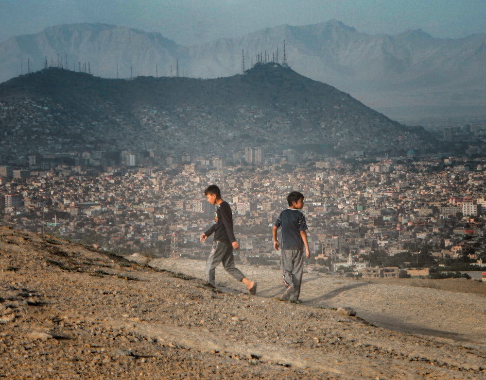two boys walking up a hill with a city in the background