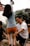 A girl is climbing a pole with the assistance of an older man who is supporting her from behind. They are outdoors, possibly in a backyard, with another child and a brick wall in the background. The scene suggests a playful and familial atmosphere.