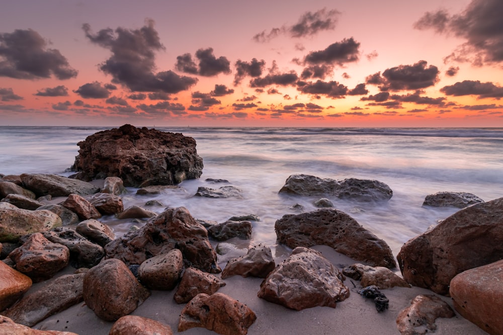 Una spiaggia rocciosa con un tramonto sullo sfondo