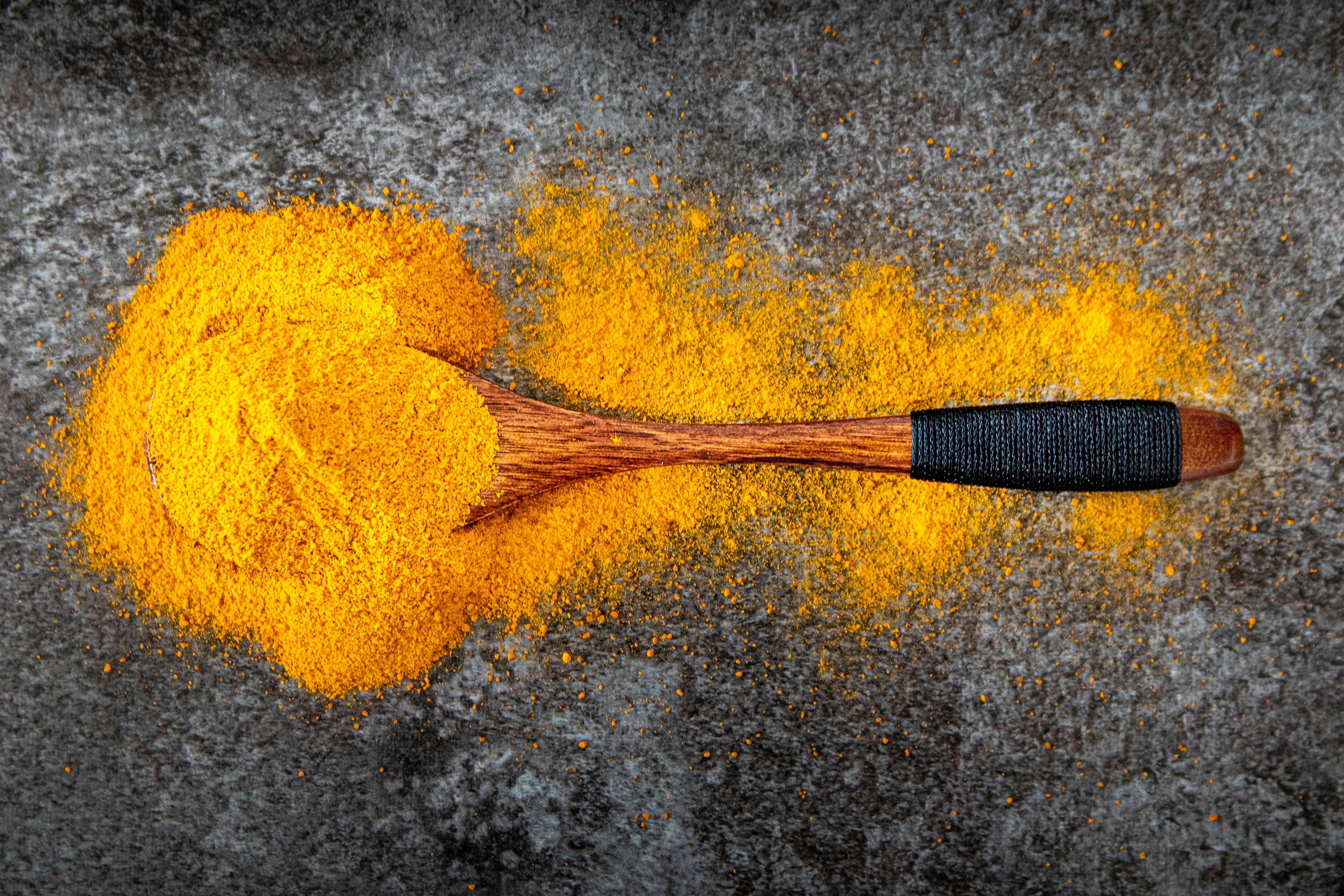Poudre de curcuma jaune vif dans une cuillère en bois sur fond rustique