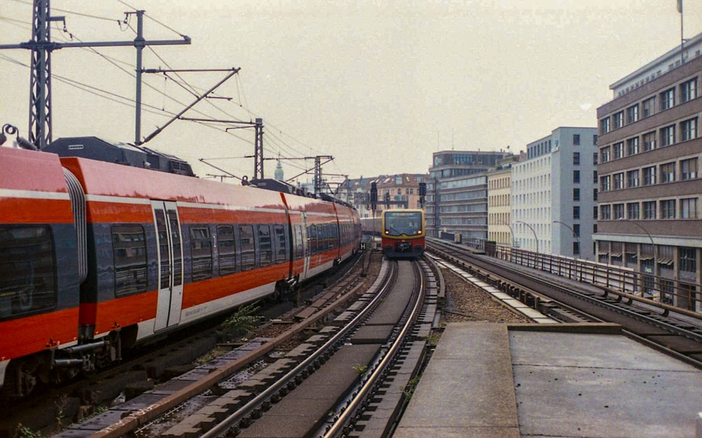 um trem vermelho viajando pelos trilhos do trem ao lado de edifícios altos