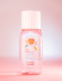 A clear plastic bottle contains a pinkish liquid and has a white cap. The label features an illustration of peaches and text in both Chinese and English, indicating it is a Peach Oolong Mouthwash. The bottle is adorned with droplets, giving a fresh, cool look while sitting against a pink gradient background.