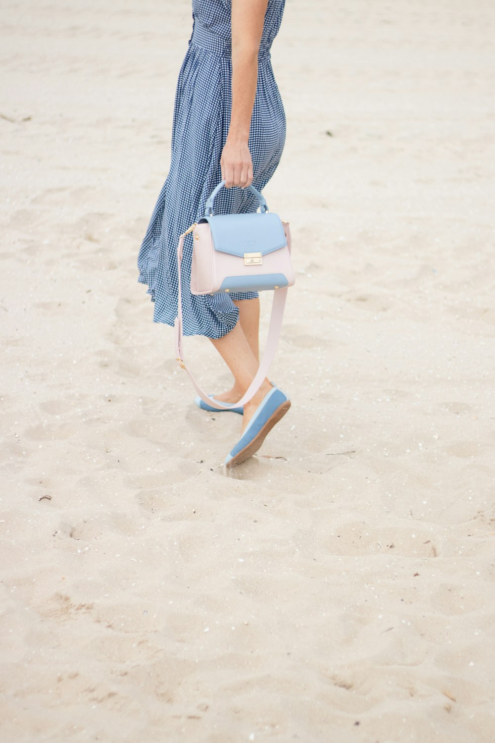 a woman walking across a sandy beach holding a purse