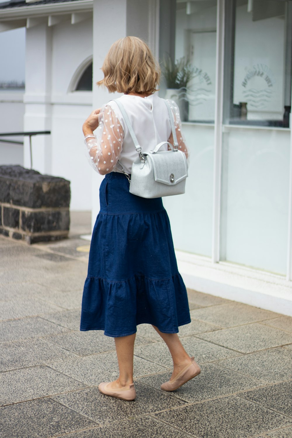 a woman walking down a sidewalk carrying a white purse