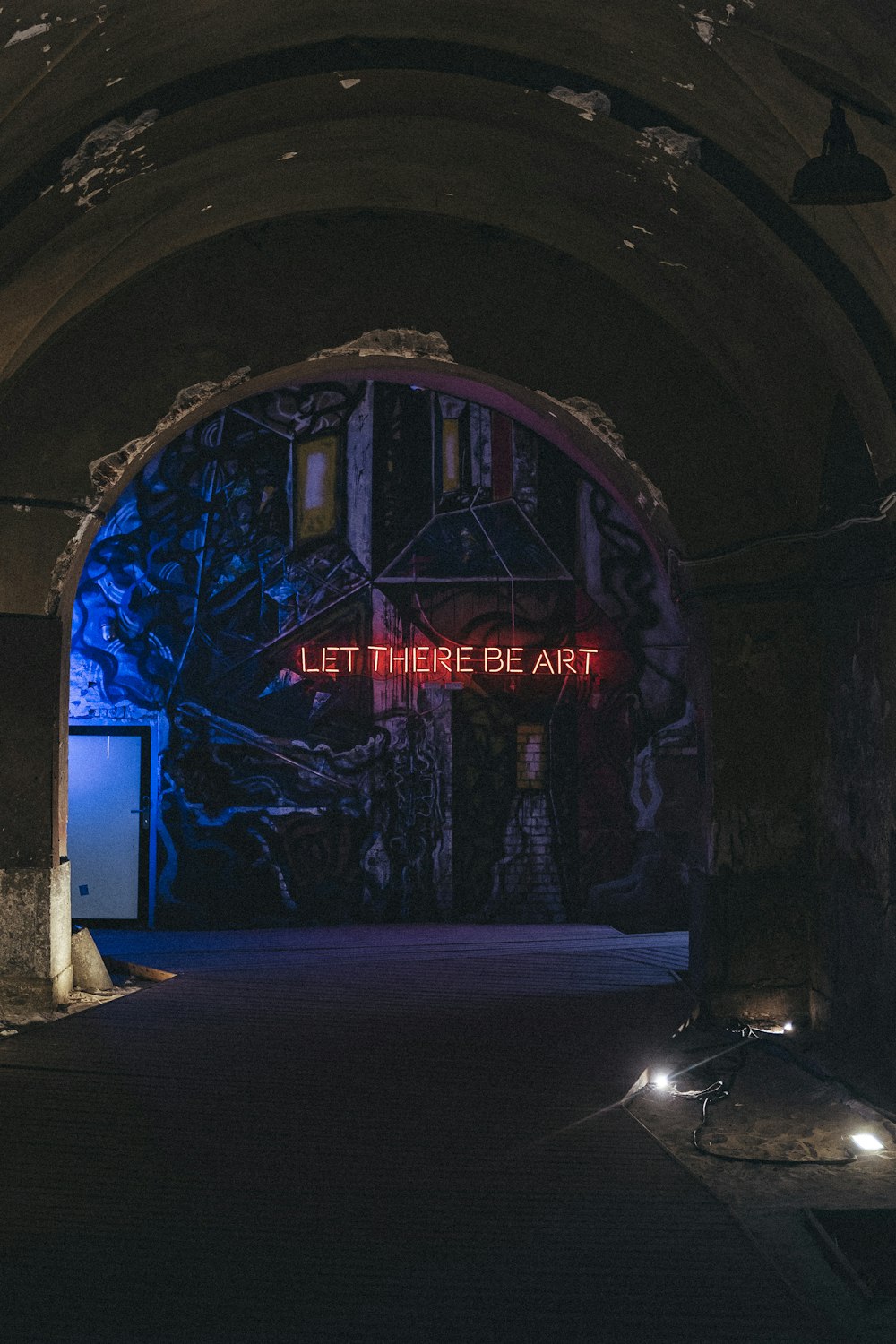 a dark tunnel with a neon sign that says let there be art