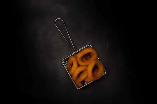 Golden onion rings and crispy bacon-topped fries served in a rustic basket.