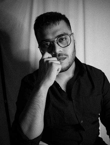 A moody black-and-white portrait of the author, pen in hand, surrounded by stacks of well-loved books.