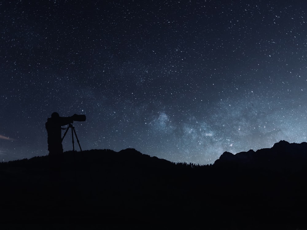 a man standing on top of a hill under a sky filled with stars