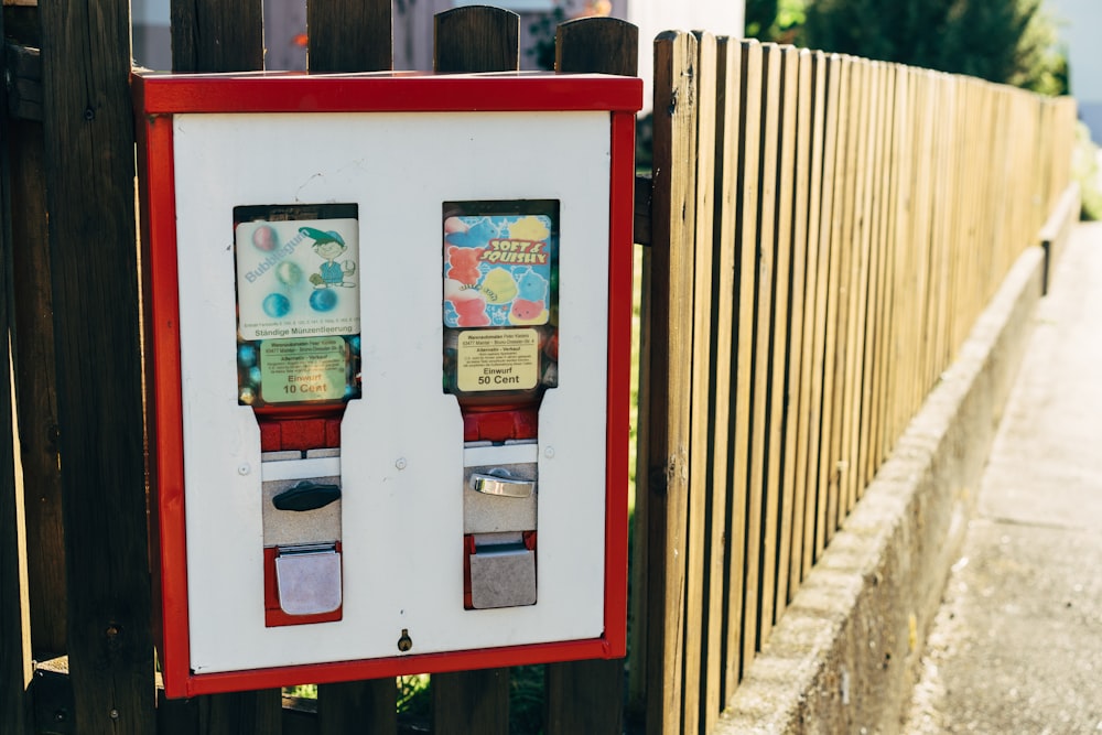 a red and white machine next to a wooden fence