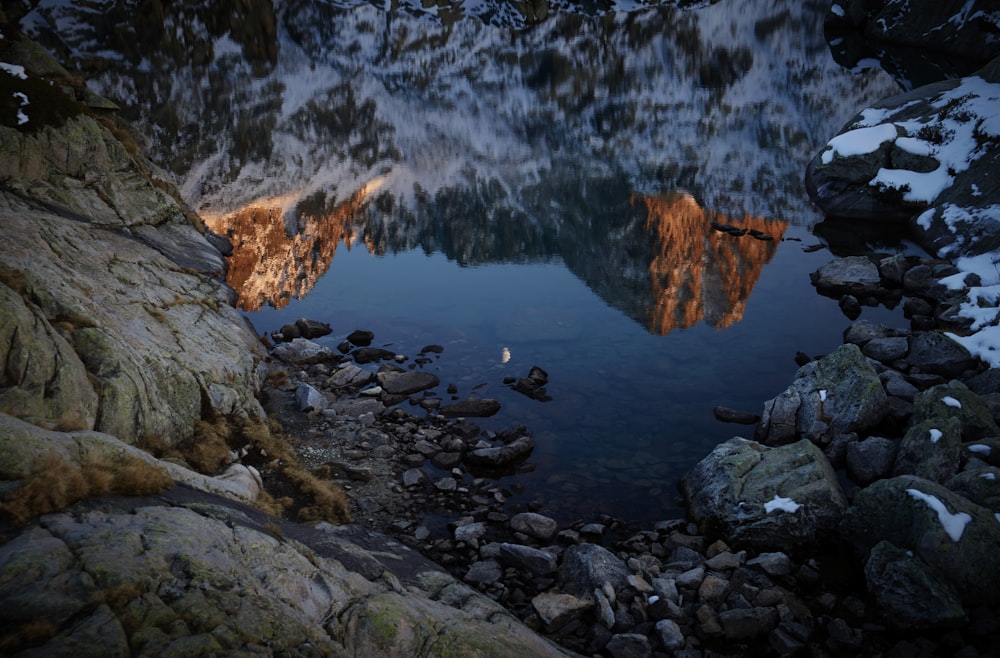 a lake surrounded by rocks and snow covered mountains