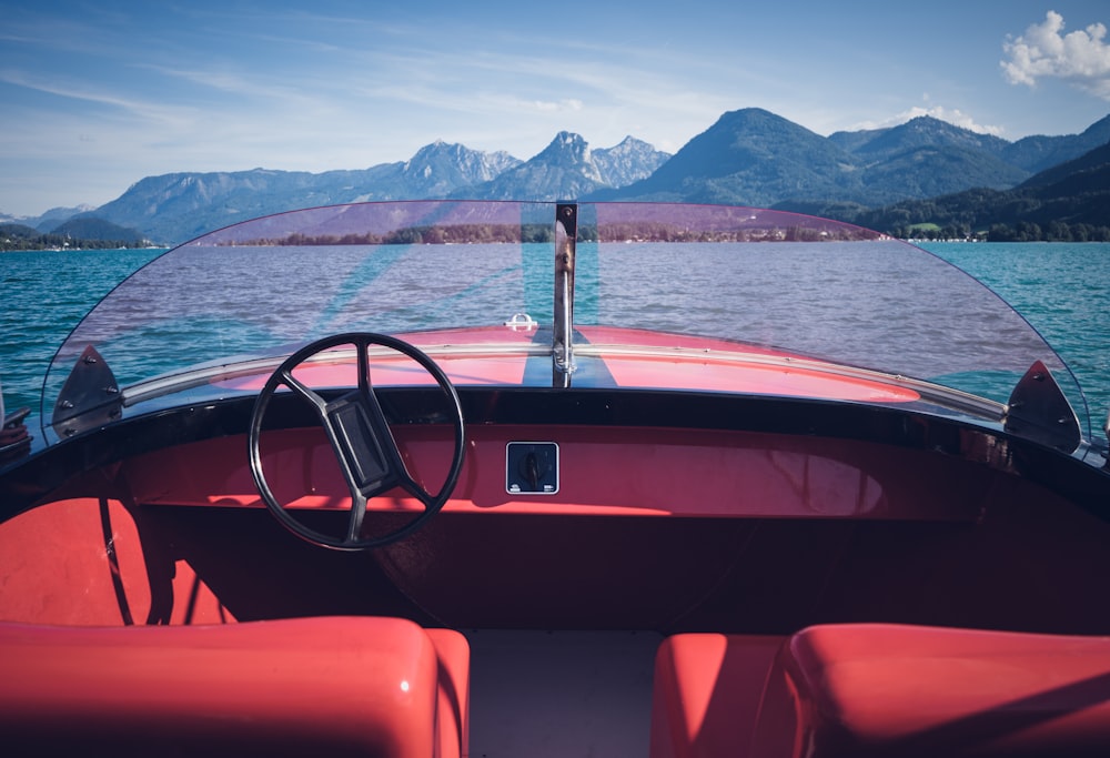 a red boat with a steering wheel on a body of water