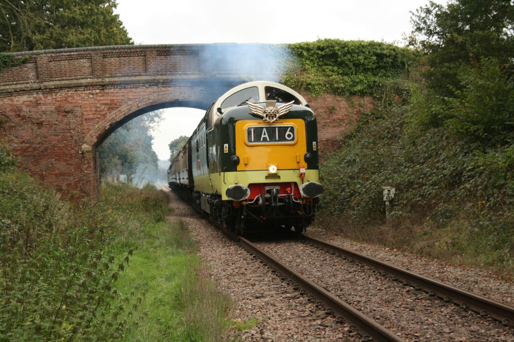 a yellow and black train traveling under a bridge