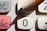 A close-up view of a calculator's keypad with a pencil poised on the number zero button. The keypad includes buttons for addition, subtraction, and an AC (all clear) function, which is highlighted in red.