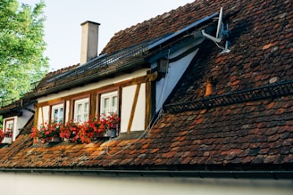 A charming house with a deep red tiled roof glowing under a sunny sky.