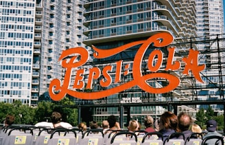 a group of people sitting in front of a pepsi cola sign
