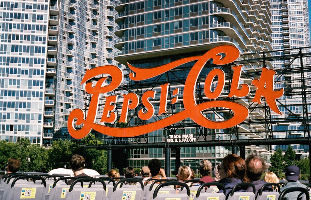 a group of people sitting in front of a pepsi cola sign