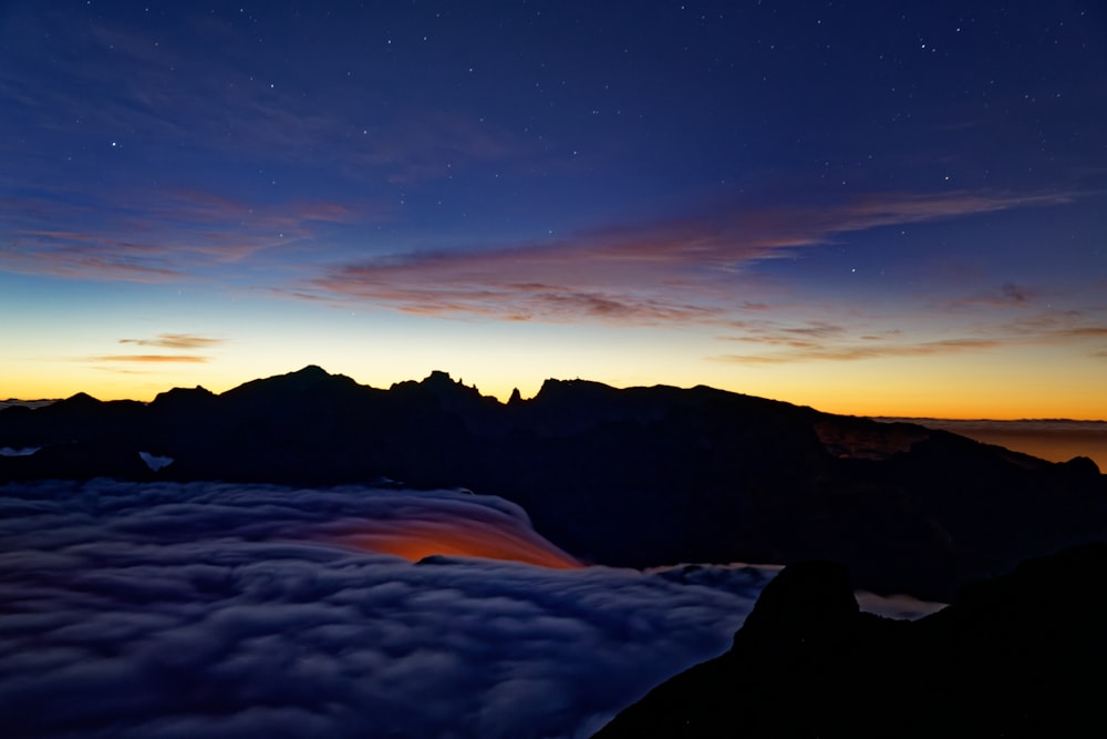 the sun is setting over the mountains above the clouds