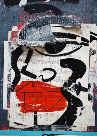 The artwork features a collage of torn and layered paper that includes sheet music and bold abstract shapes. Prominent black lines form the outline of a face with exaggerated features, such as large lips painted in vivid red. The background is a mix of distressed textures, blending gray, black, and hints of red, creating a sense of urban decay.