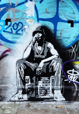 A graffiti artwork of a person wearing a hat and a large chain, sitting on a stereo or boombox. The background features colorful graffiti with patterns and numbers.