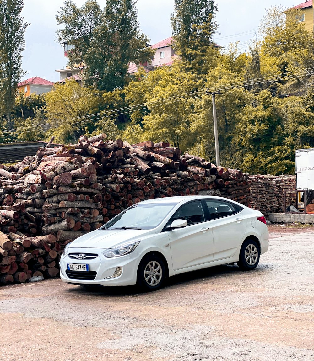 a white car parked in front of a pile of wood