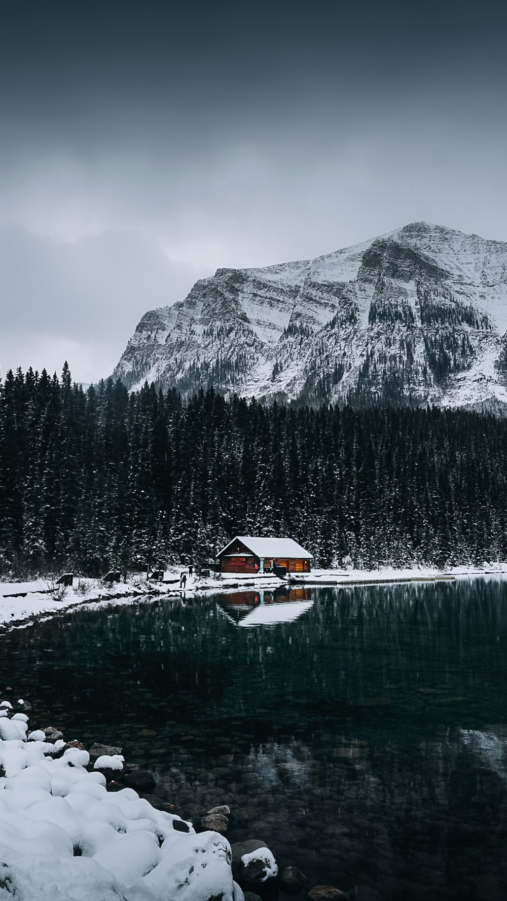 a small cabin sits on the shore of a mountain lake