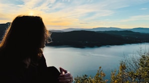 a woman standing on top of a mountain next to a lake