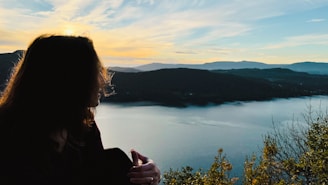 a woman standing on top of a mountain next to a lake