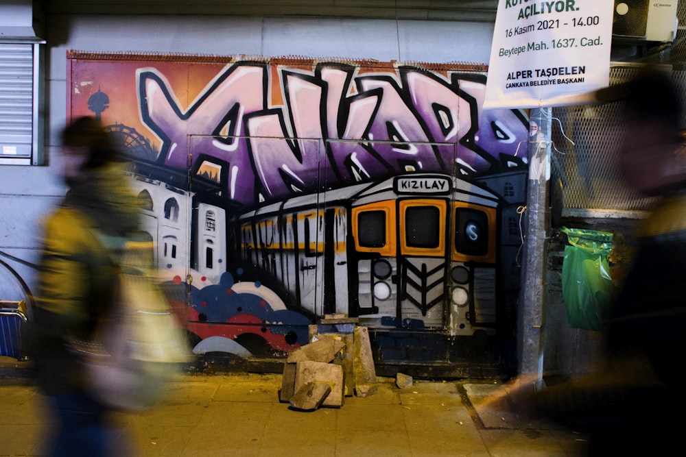 people walking past a wall with graffiti on it