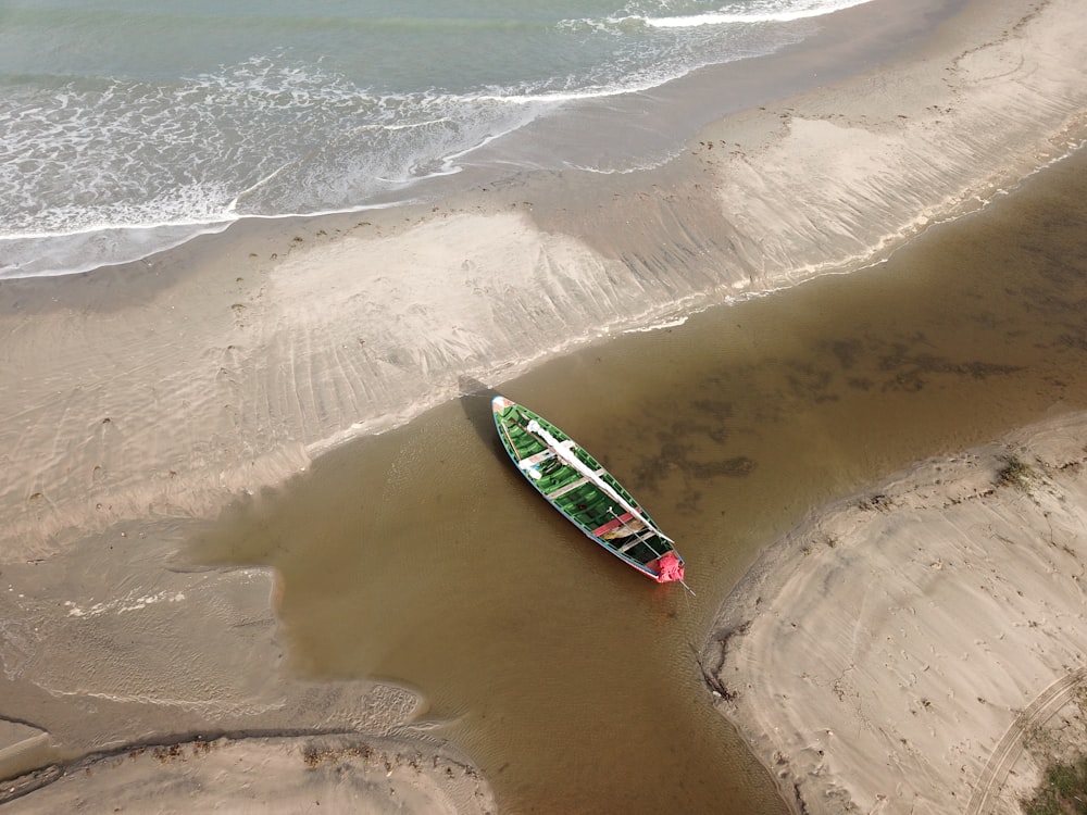 a green and red boat sitting on top of a sandy beach