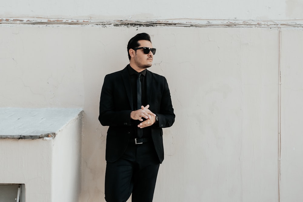 a man in a suit and sunglasses leaning against a wall