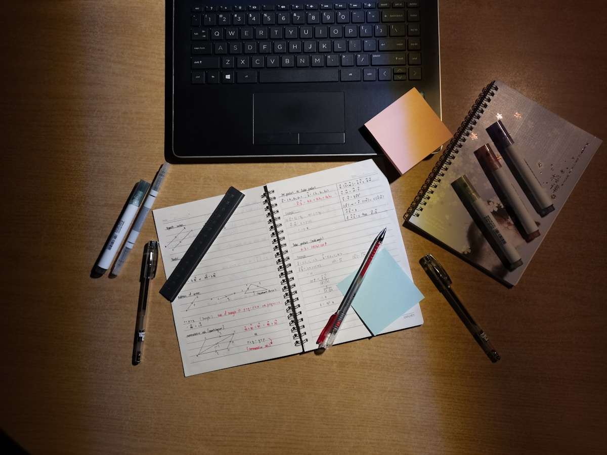 A college student working on a laptop at a wooden desk, planning a mentoring program for K-12 students.