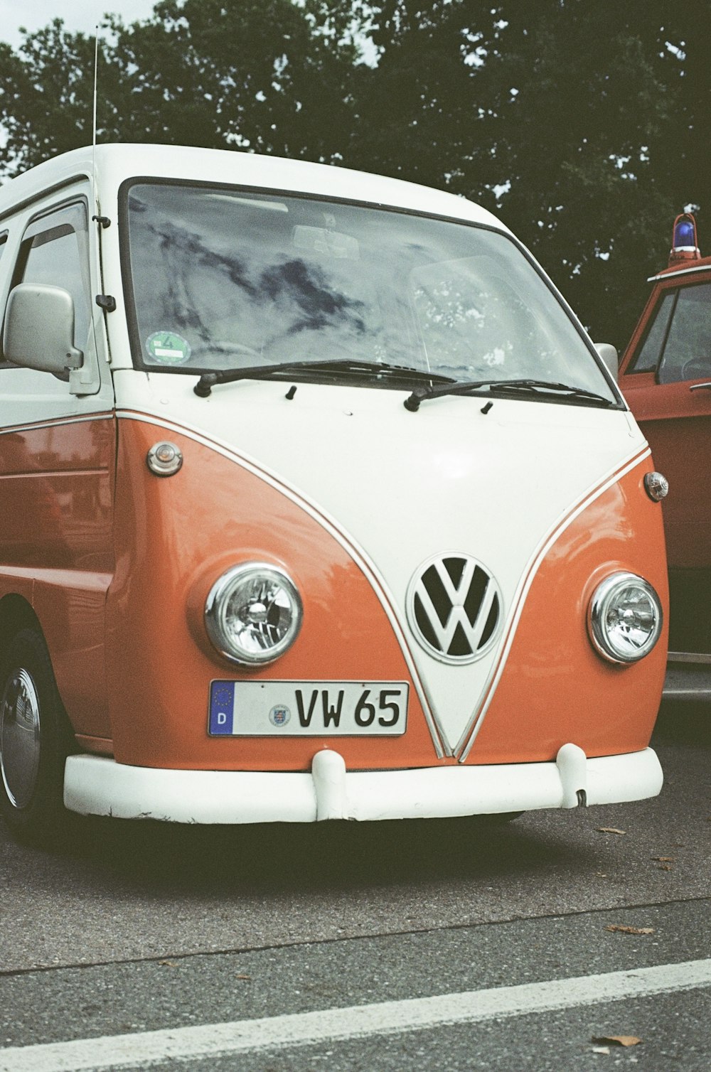 Un autobus VW arancione e bianco parcheggiato accanto a un'auto rossa