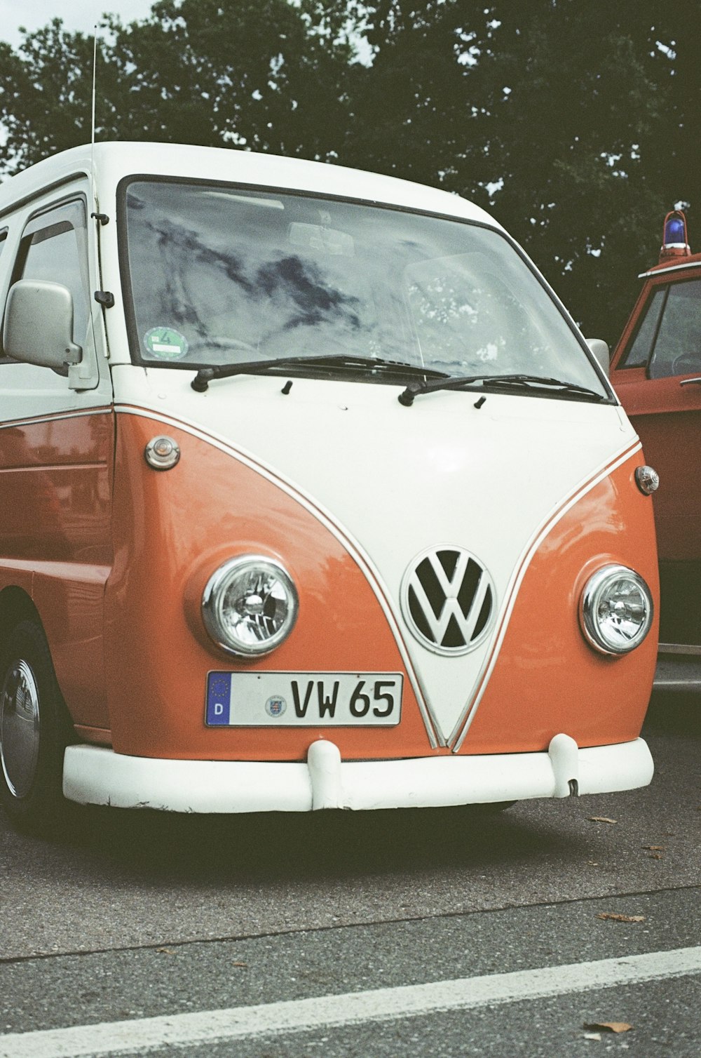 an orange and white vw bus parked next to a red car