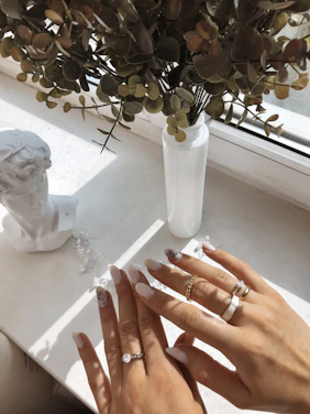 Close-up of hands wearing delicate, modern rings and bracelets bathed in soft natural light.