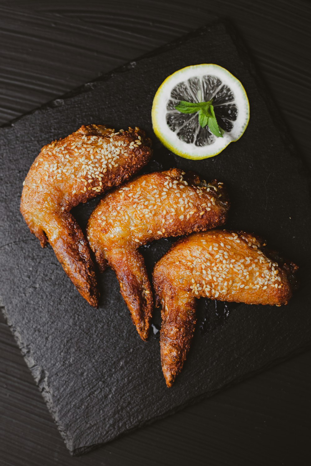 fried chicken wings with a half of a grapefruit on a slate board