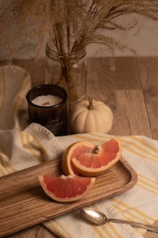 a grapefruit cut in half on a cutting board, white pumpkin and a scented candle on a wooden table