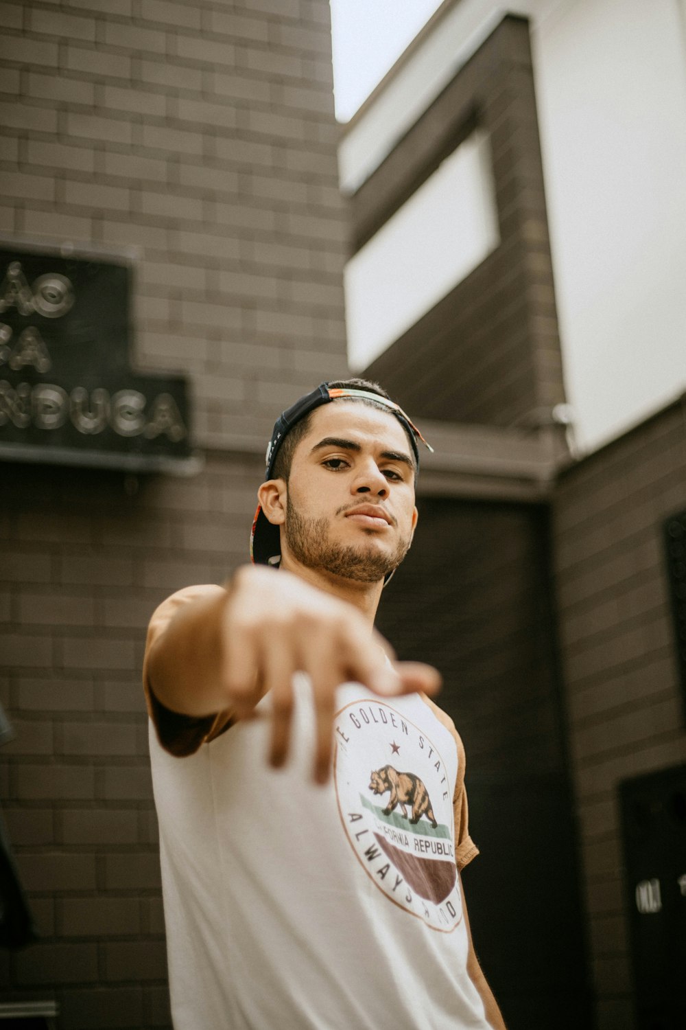 a man pointing at the camera with a brick building in the background