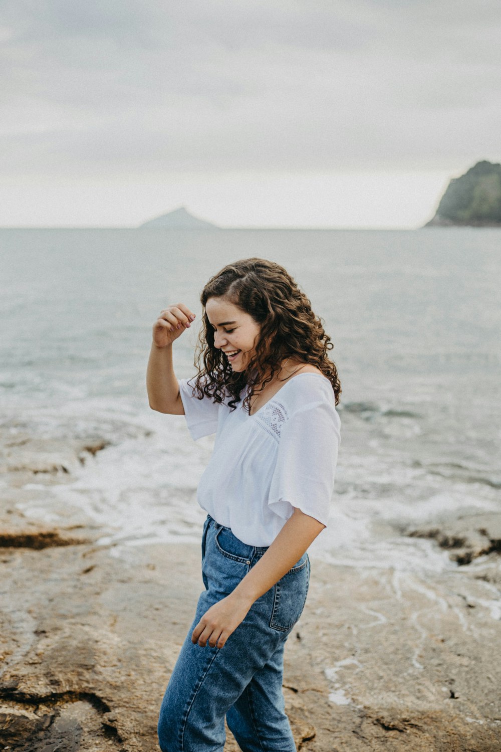 a woman standing on a rocky beach next to the ocean